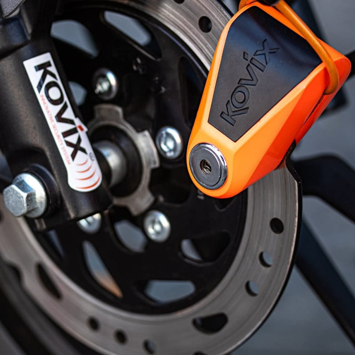 Candado de disco Kovix naranja en rueda delantera de motocicleta para máxima seguridad antirrobo